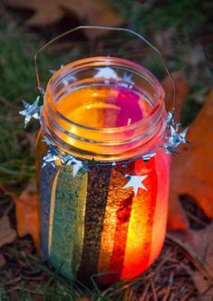 a jar filled with colorful liquid sitting on top of grass next to leaves and fallen leaves