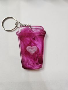 a glass jar with a heart in it on a white tableclothed surface is being held by a metal keychain