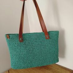 a green crocheted bag sitting on top of a wooden table next to a white wall