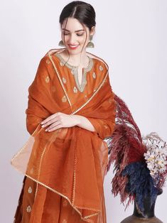 Indulge in timeless elegance with this rust kurta set. Its luxurious silk kurta is accentuated with delicate zari embroidery, while the cotton silk pants and organza dupatta are finished with exquisite gota work. A truly regal ensemble to make you feel like royalty. No. of pieces - 3 piece set. Fabric - Silk, Cotton Silk and Oraganza. Color - Rust. Kurta Length - 44 inches. Washing Instructions - Dry Clean. Transitional Orange Straight Kurta Sets, Traditional Long Sleeve Tissue Silk Kurta, Festival Tissue Silk Straight Kurta, Transitional Orange Zari Work Kurta, Orange Bollywood Kurta For Transitional Season, Festive Traditional Tissue Silk Kurta, Traditional Orange Palazzo Set With Straight Kurta, Traditional Orange Palazzo Set For Festive Occasions, Traditional Orange Palazzo Set For Festive Season