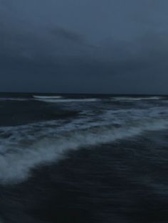 the ocean is dark and choppy with waves coming in to shore on a cloudy night