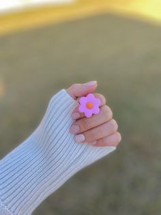 a person holding a small pink flower in their left hand and wearing a white sweater