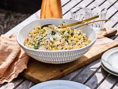 a white bowl filled with food sitting on top of a wooden table next to plates and utensils