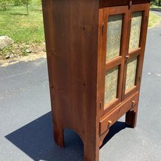 an old wooden cabinet with glass doors in the middle of a parking lot next to a grassy area