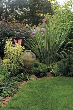 a garden with lots of green grass and plants in it, along with a stone planter