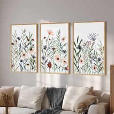 three floral paintings hang on the wall above a couch