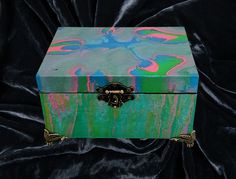 a colorful box sitting on top of a black velvet covered surface with gold trimming