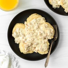 two black plates topped with biscuits and gravy next to a glass of orange juice