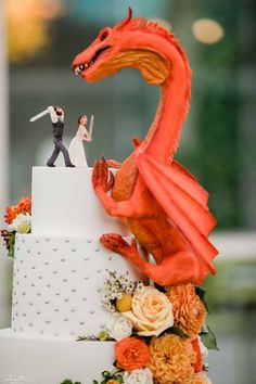 a wedding cake with a red dragon figurine on top and an orange flower arrangement