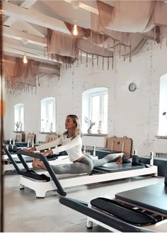 a woman is sitting on an exercise mat in the middle of a room filled with yoga mats