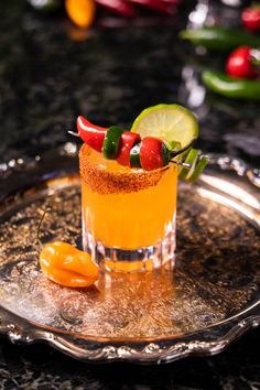 a small glass filled with an orange drink and garnished with chili peppers, limes and jalapenos