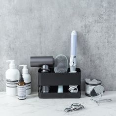 an assortment of personal care items in a black holder on a marble countertop with scissors, shaving razors and toothbrushes