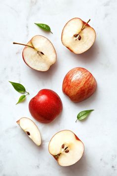 an apple sliced in half and sitting on a marble counter top with leaves around it