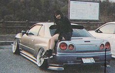 a man sitting on the hood of a car in front of two other parked cars