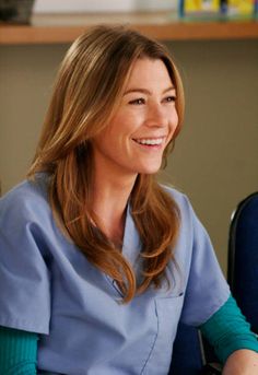 a smiling woman in scrubs sitting at a desk