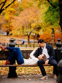 a man and woman sitting on a park bench in the fall with leaves all around them