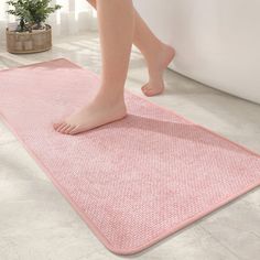 a woman's bare feet are standing on a pink rug in front of a white bathtub