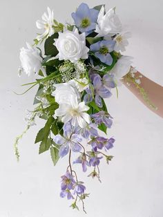 a bouquet of white and blue flowers is being held up by someone's hand