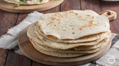 a stack of tortillas sitting on top of a wooden plate next to other food items