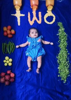 a baby is laying on a blue blanket surrounded by fruits and vegetables that spell out