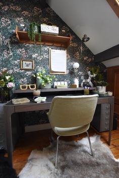 a desk with a chair in front of it and a wallpapered wall behind it