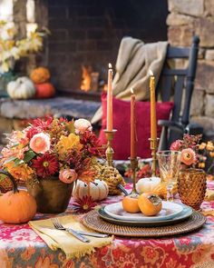 a table set with pumpkins, flowers and candles in front of a fire place