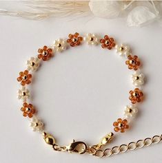 a bracelet with orange and white beads is shown on a table next to a flower