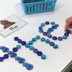 a child's hand writing the word hne on a table with blue beads