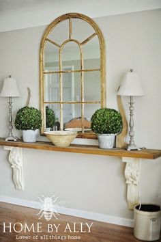 there is a mirror and some plants on the mantle in this living room with wood flooring