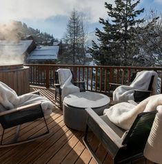 two lounge chairs on a deck with snow covered trees in the background and steam rising from the back