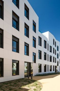 an apartment building with many windows and grass in the foreground, on a sunny day