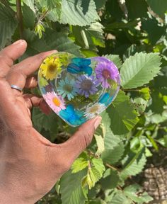 a hand holding a glass ball with flowers in it and green leaves around the globe