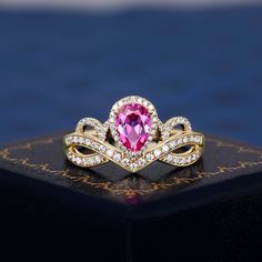 a pink heart shaped diamond ring sitting on top of a black box with gold trimmings