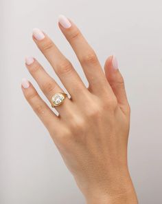 a woman's hand wearing a gold ring with a white diamond on the middle