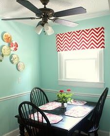 a dining room table with four chairs and a ceiling fan in the corner, along with plates on the wall