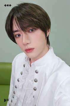 a young man with short hair wearing a white shirt and black pants sitting on a green couch