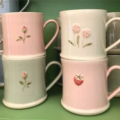 three coffee mugs with pink flowers and hearts painted on them sitting next to each other