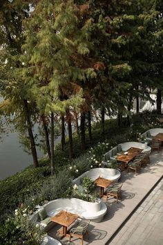 tables and chairs are lined up along the water's edge with trees in the background