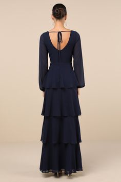 the back of a woman wearing a blue dress with long sleeves and tiered layers