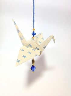 an origami crane hanging from a string on a white wall with blue beads