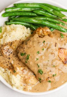 a white plate topped with meat and gravy next to green beans