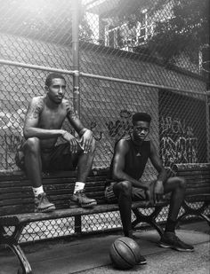 two men sitting on a bench in front of a basketball ball and chain link fence