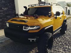 a yellow truck parked on the side of a road next to a white building and brick wall