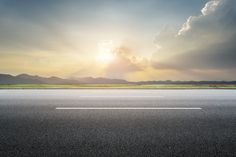 the sun is setting on an empty highway with mountains in the background and clouds above