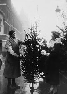 an old black and white photo of two women decorating a christmas tree