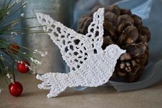 a white crocheted bird sitting next to a pine cone