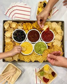 two hands reaching for chips and salsa in a tray