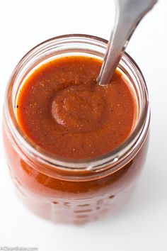 a jar filled with sauce and a spoon sticking out of the top, on a white surface