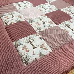 a pink and white quilted bed with trees in the middle on top of it