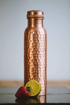 a strawberry and lime sitting next to a copper bottle